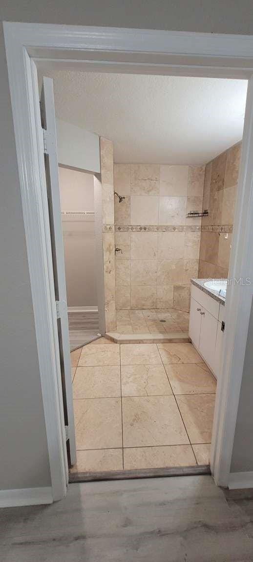 full bath featuring a textured ceiling, tiled shower, and vanity