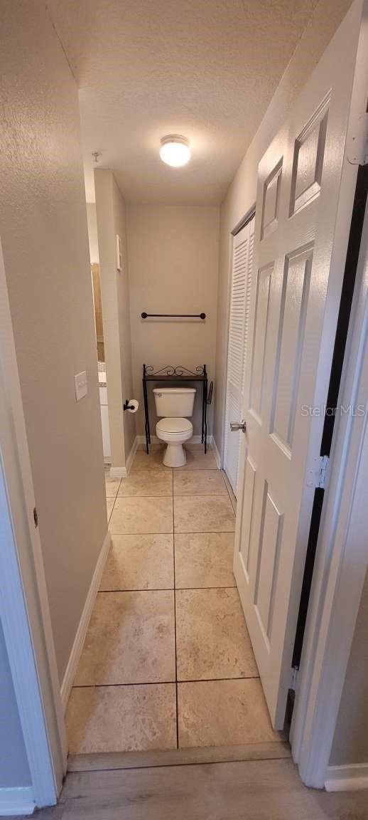 bathroom featuring baseboards, a textured ceiling, toilet, and tile patterned floors