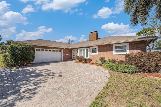 ranch-style home with a garage, a chimney, decorative driveway, and brick siding