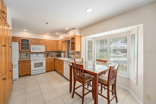 kitchen featuring white appliances, glass insert cabinets, light countertops, and a sink