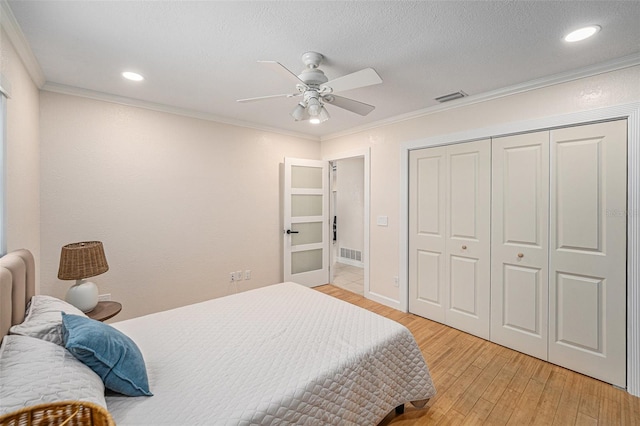 bedroom with ornamental molding, visible vents, a textured ceiling, and light wood finished floors