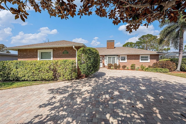 single story home featuring decorative driveway, brick siding, and a chimney