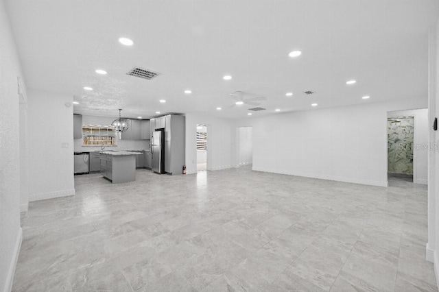 unfurnished living room featuring recessed lighting, visible vents, baseboards, and ceiling fan with notable chandelier