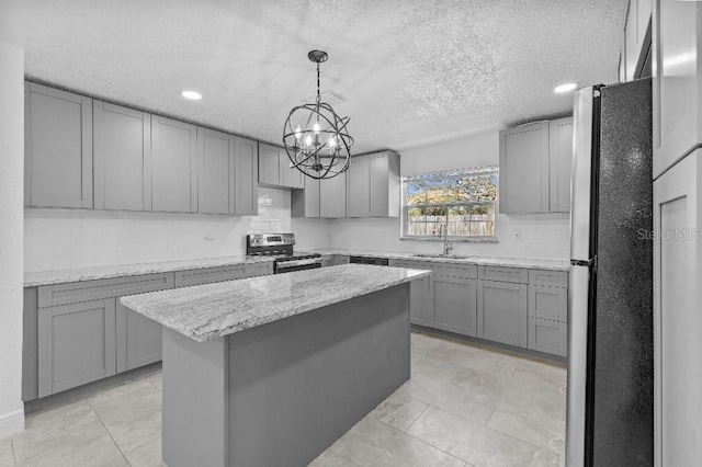 kitchen with light stone counters, gray cabinetry, stainless steel appliances, a kitchen island, and a sink