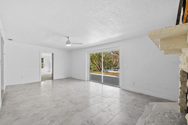 unfurnished living room with a textured ceiling, ceiling fan, a stone fireplace, and baseboards