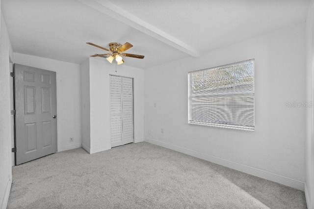 unfurnished bedroom featuring carpet, beam ceiling, a closet, a ceiling fan, and baseboards