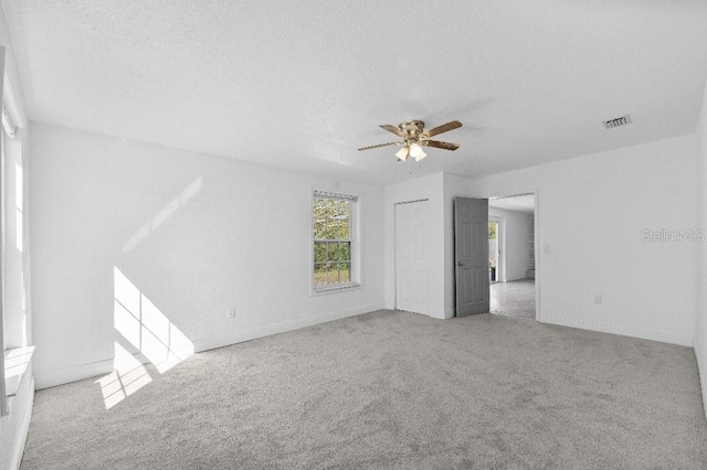 empty room with a textured ceiling, carpet floors, visible vents, baseboards, and a ceiling fan