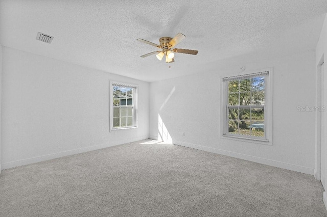 unfurnished room featuring a textured ceiling, carpet floors, visible vents, baseboards, and a ceiling fan