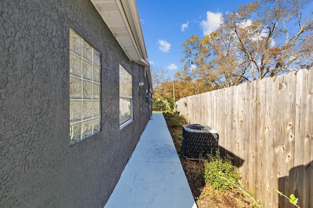 view of side of property featuring fence, central AC unit, and stucco siding