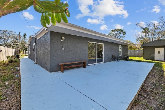 back of house with an outbuilding, a patio, fence, and stucco siding