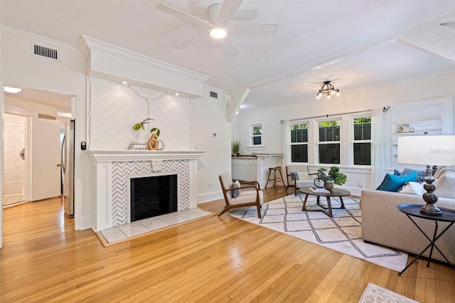 living room featuring a tile fireplace, visible vents, crown molding, and hardwood / wood-style flooring