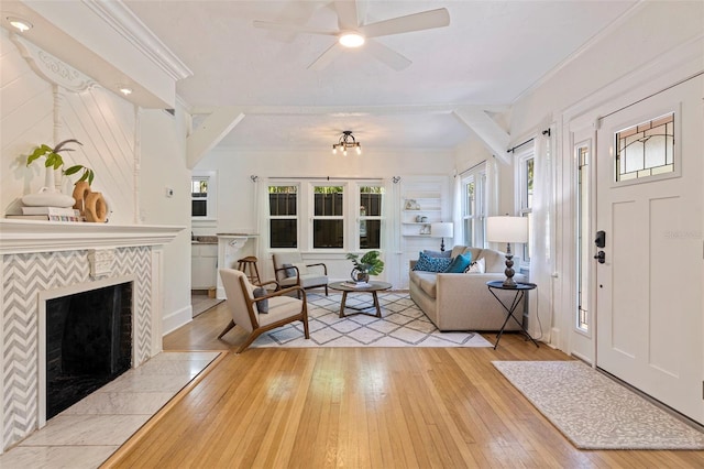 living room with light wood finished floors, a tile fireplace, a ceiling fan, and crown molding