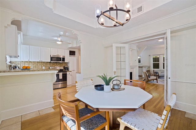 dining space with a tray ceiling, a fireplace, visible vents, light wood-style floors, and ornamental molding