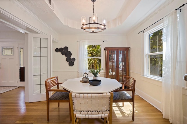 dining area featuring ornamental molding, a tray ceiling, light wood-style flooring, and an inviting chandelier