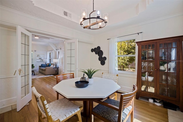 dining area featuring french doors, a notable chandelier, visible vents, light wood-style floors, and ornamental molding