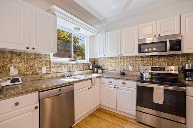 kitchen with appliances with stainless steel finishes, white cabinets, a sink, and decorative backsplash