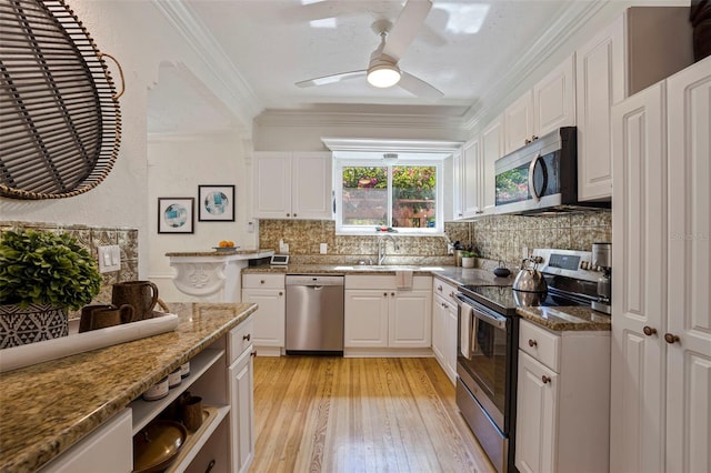 kitchen with a sink, white cabinets, ornamental molding, appliances with stainless steel finishes, and tasteful backsplash