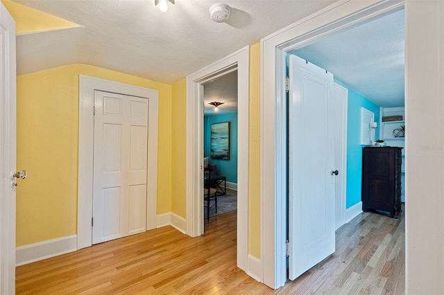 corridor with light wood-style floors, a textured ceiling, and baseboards