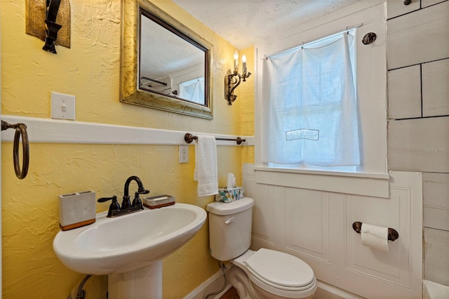 bathroom with toilet, a textured wall, a sink, and a wealth of natural light