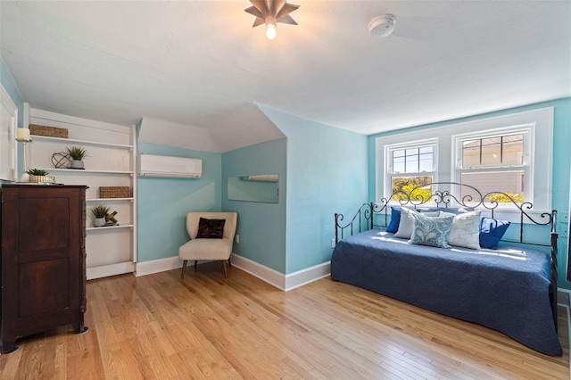 bedroom featuring light wood-type flooring, baseboards, and an AC wall unit