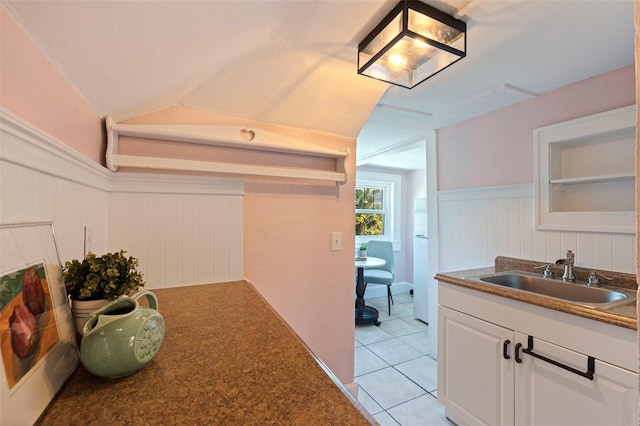 interior space with light tile patterned floors, white cabinets, a wainscoted wall, vaulted ceiling, and a sink