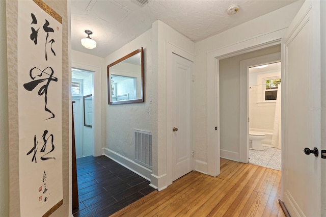 hall featuring wood finished floors, visible vents, and baseboards