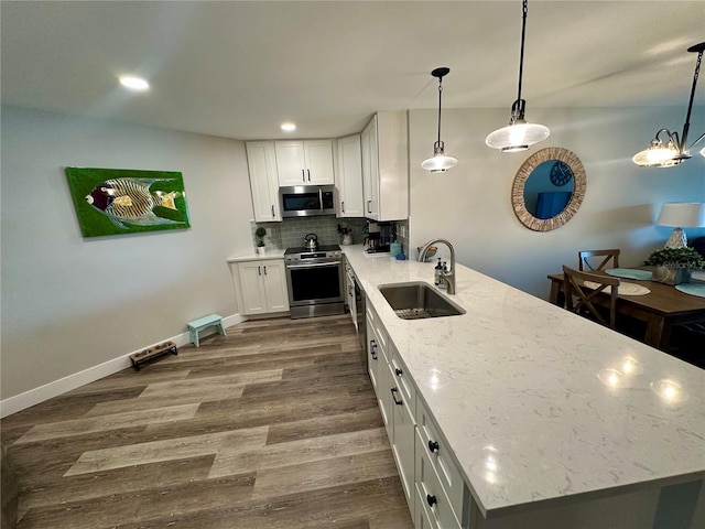 kitchen with stainless steel appliances, a peninsula, a sink, dark wood-style floors, and tasteful backsplash