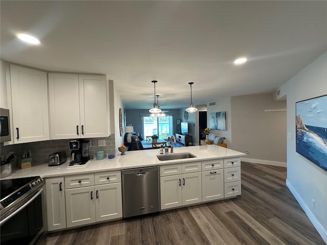 kitchen featuring decorative backsplash, dark wood-style floors, appliances with stainless steel finishes, a peninsula, and a sink