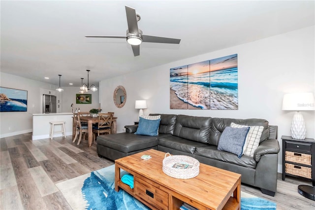 living area featuring light wood finished floors, baseboards, and ceiling fan with notable chandelier