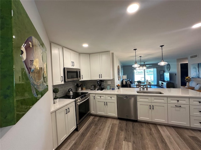 kitchen with a peninsula, dark wood-style flooring, a sink, visible vents, and appliances with stainless steel finishes