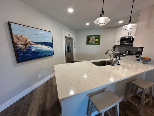 kitchen featuring light stone counters, stainless steel appliances, white cabinets, a sink, and a peninsula