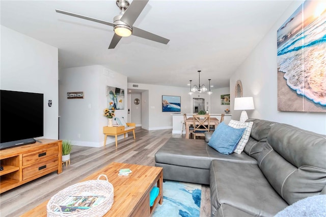 living room with light wood-type flooring, visible vents, baseboards, and ceiling fan with notable chandelier