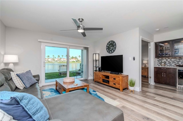 living room featuring light wood finished floors, baseboards, a ceiling fan, wine cooler, and a bar