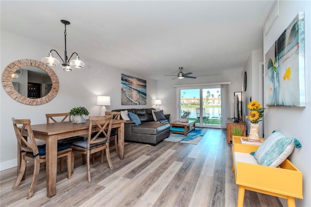 dining room featuring ceiling fan with notable chandelier, light wood-type flooring, and baseboards