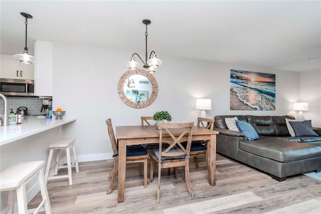 dining space featuring light wood-style flooring, baseboards, and a notable chandelier