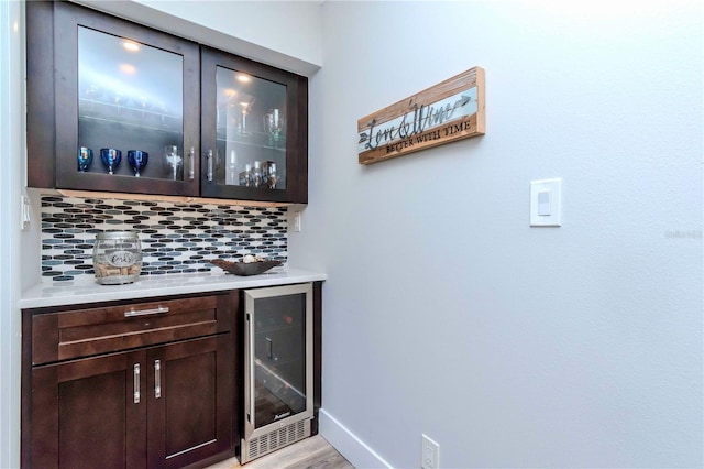 bar featuring wine cooler, baseboards, light wood-type flooring, backsplash, and a dry bar