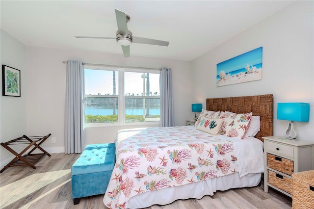 bedroom featuring ceiling fan, light wood finished floors, a water view, and baseboards