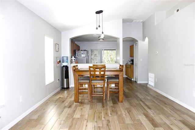 dining area featuring light wood finished floors, arched walkways, baseboards, and lofted ceiling