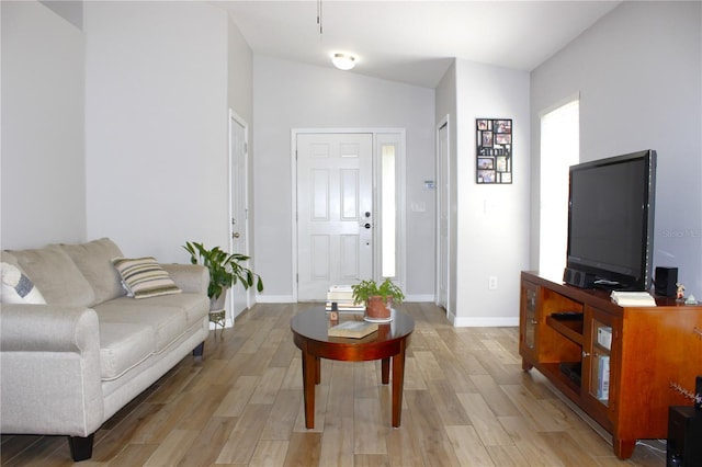 living area featuring baseboards, light wood-style flooring, and vaulted ceiling