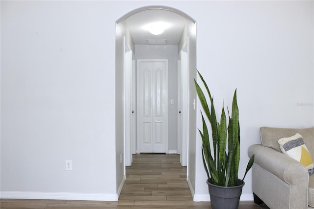 corridor featuring arched walkways, visible vents, light wood finished floors, and baseboards