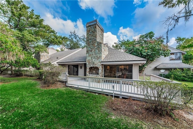 back of property with a shingled roof, a chimney, a deck, and a yard