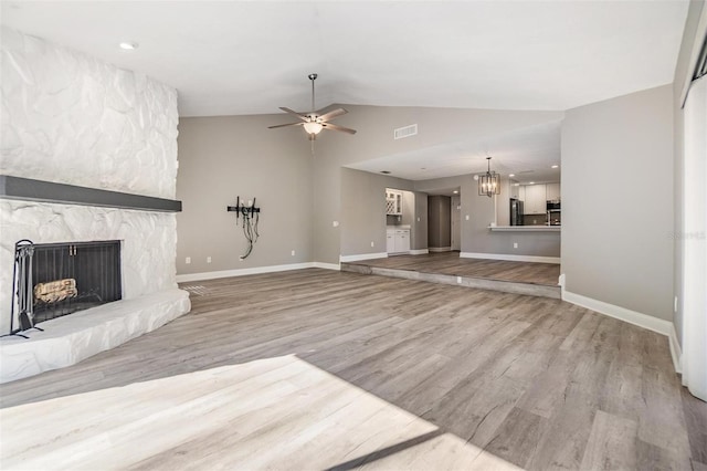 unfurnished living room featuring wood finished floors, visible vents, lofted ceiling, a stone fireplace, and ceiling fan with notable chandelier