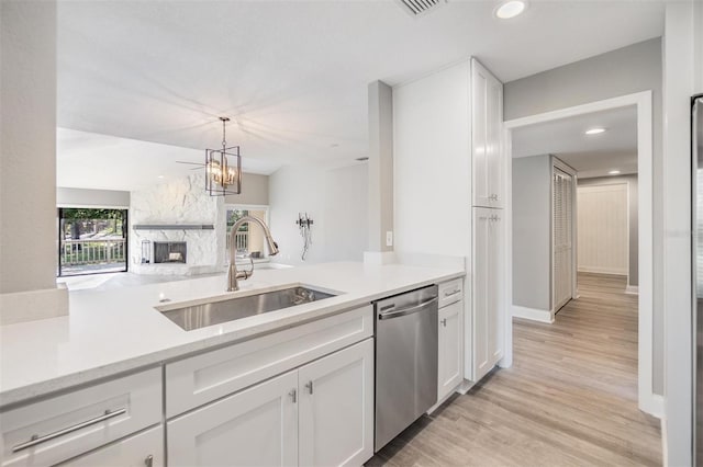 kitchen with dishwasher, a stone fireplace, white cabinetry, and a sink