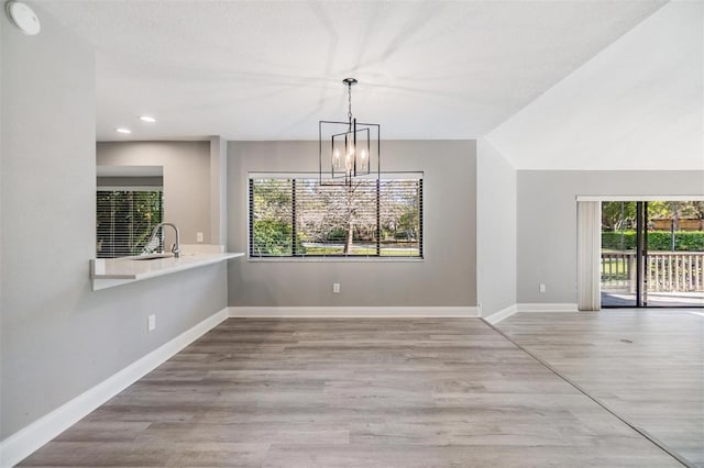 unfurnished dining area with an inviting chandelier, wood finished floors, baseboards, and a sink