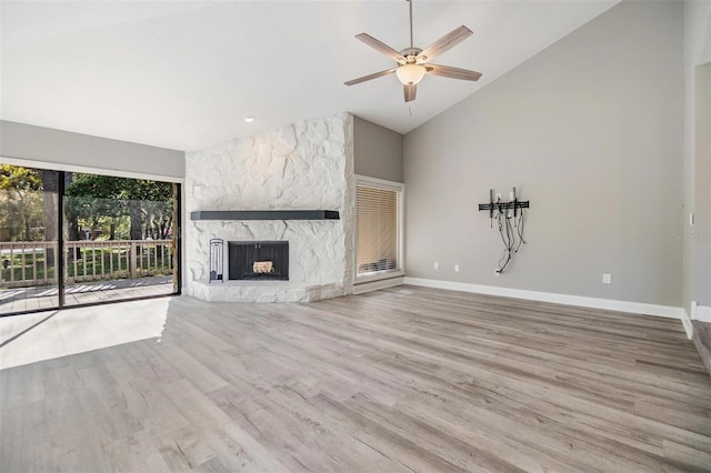 unfurnished living room featuring a stone fireplace, high vaulted ceiling, baseboards, and wood finished floors