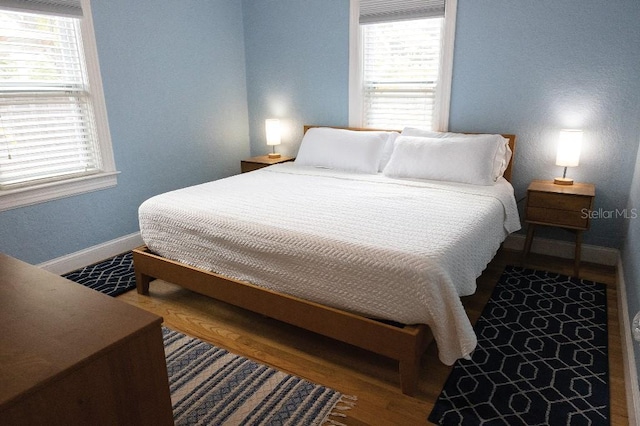 bedroom with multiple windows, baseboards, and wood finished floors