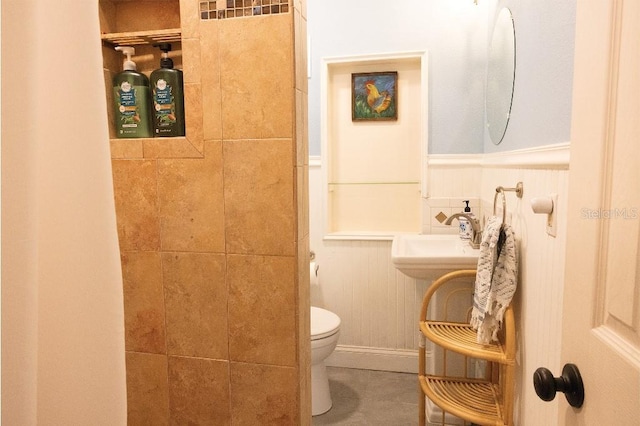 bathroom featuring tiled shower, wainscoting, a sink, and toilet