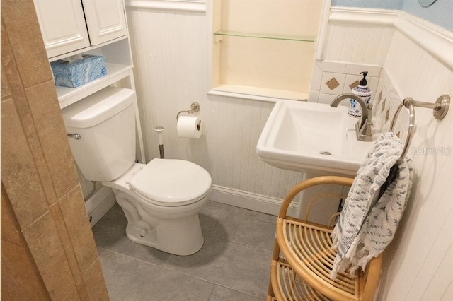 half bath featuring a wainscoted wall, a sink, toilet, and tile patterned floors