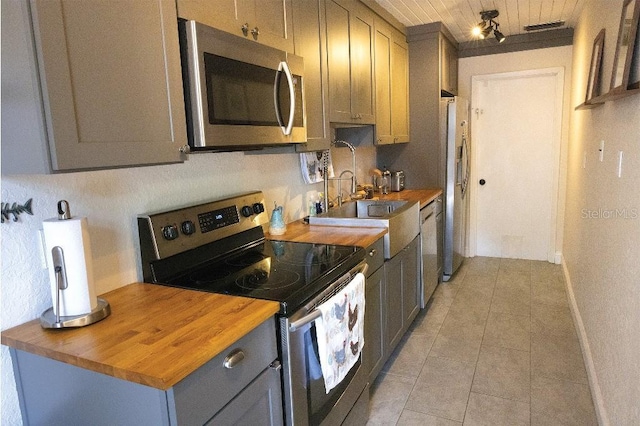 kitchen with light tile patterned floors, baseboards, butcher block counters, stainless steel appliances, and gray cabinetry