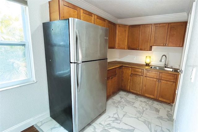 kitchen with marble finish floor, brown cabinets, a sink, and freestanding refrigerator